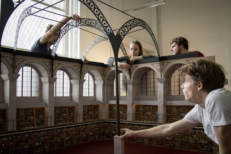 People discussing ideas inside a library-like interior, representing editorial research and collaboration.